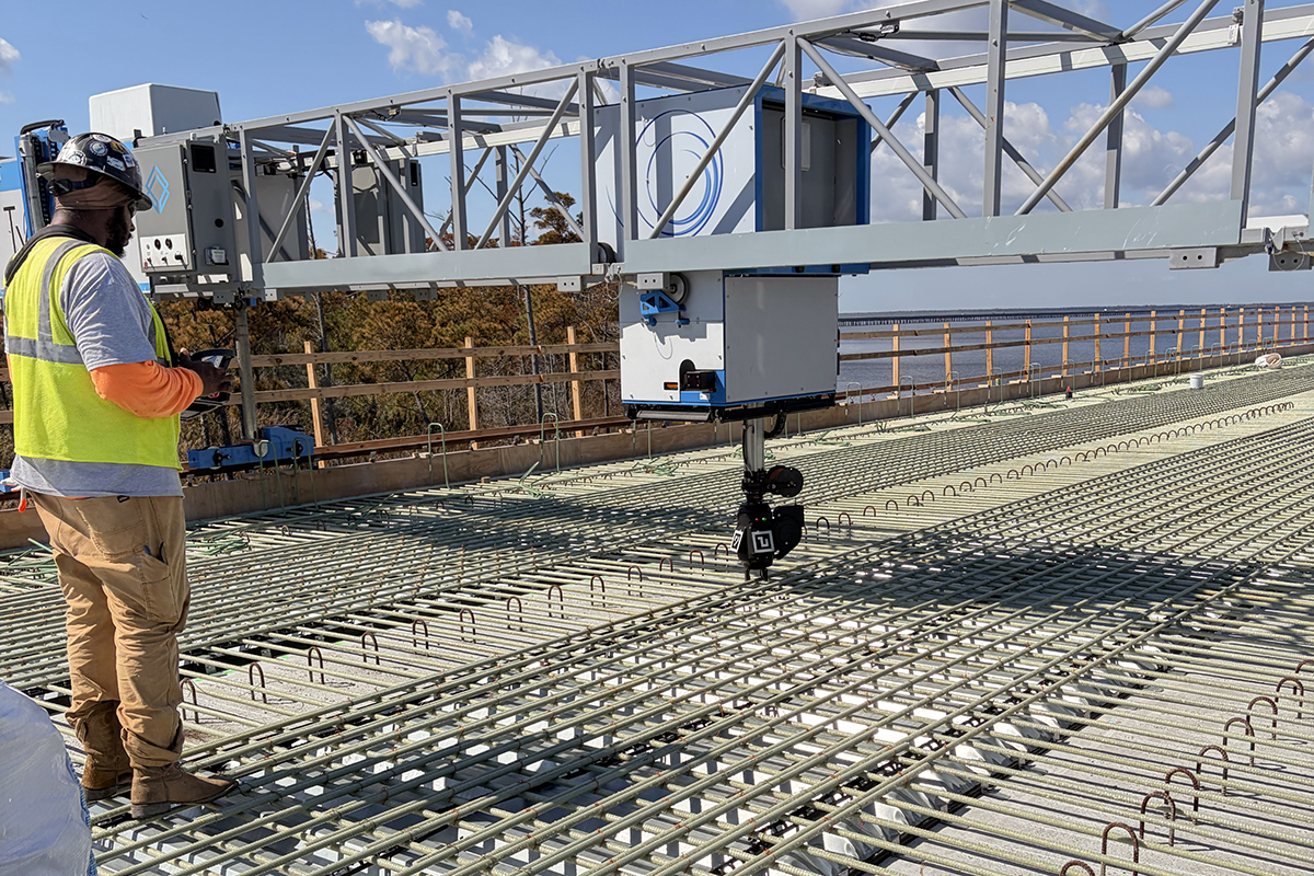 A bridge construction worker watches Tybot, an autonomous robot, tie rebar together. Photo: Kip Tabb